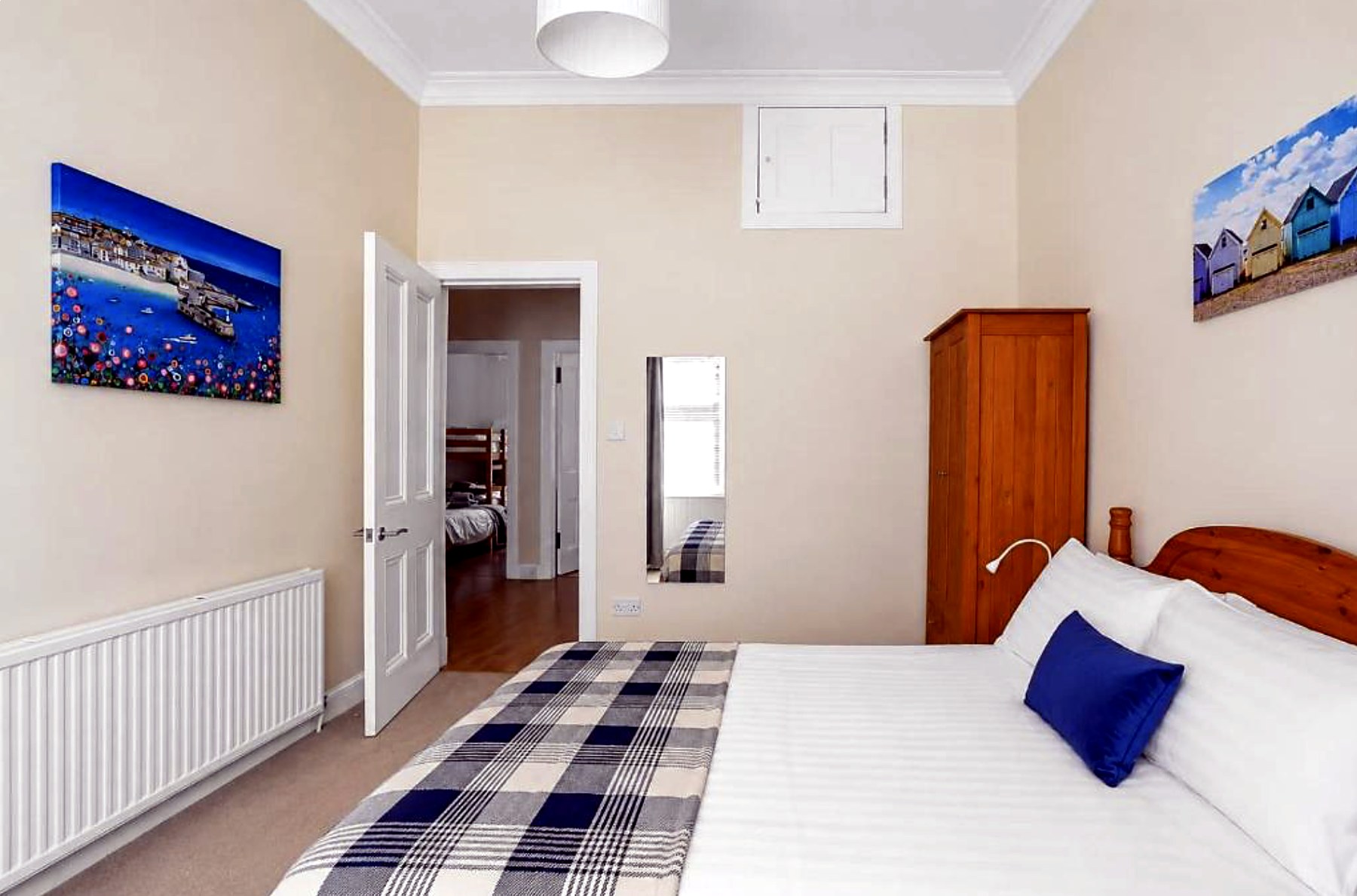 Second bedroom at Above the Bay with tartan throw, pine wardrobe and coastal canvas prints
