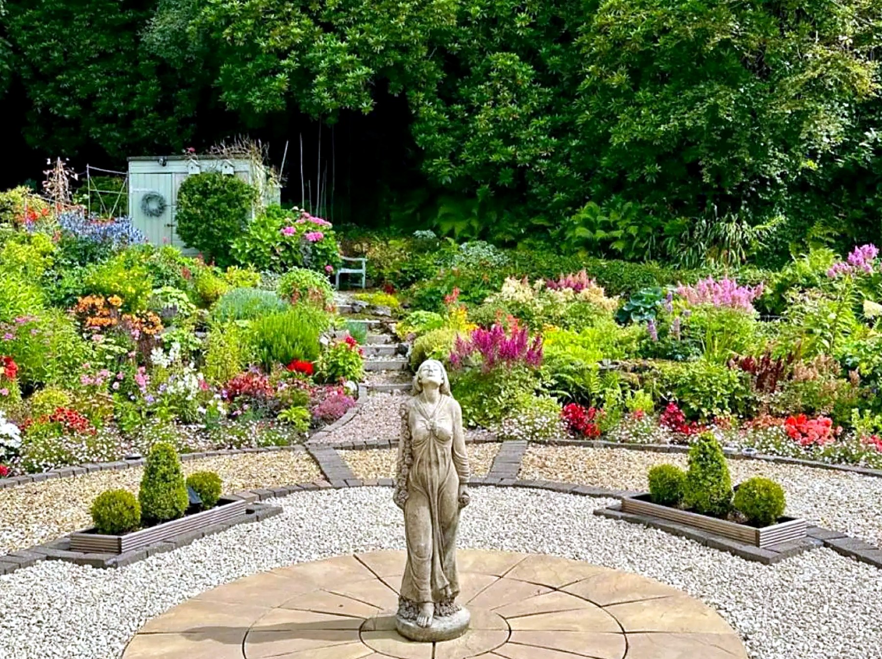 The planted rear garden at Highlander House with a stone statue and gravel paths