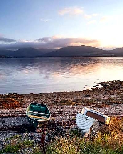 Two rowing boats pulled up on a Bute shingle beach at dawn, with the hills across the water