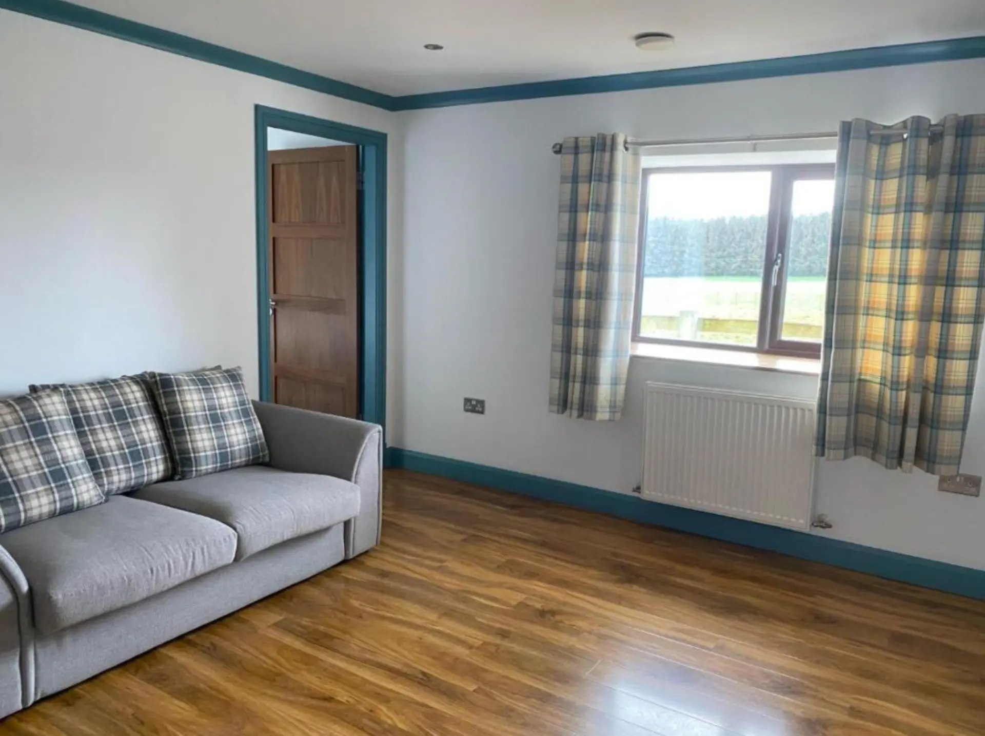 A bright sitting room at the Kingarth Hotel with a grey sofa, tartan cushions and a window over the fields