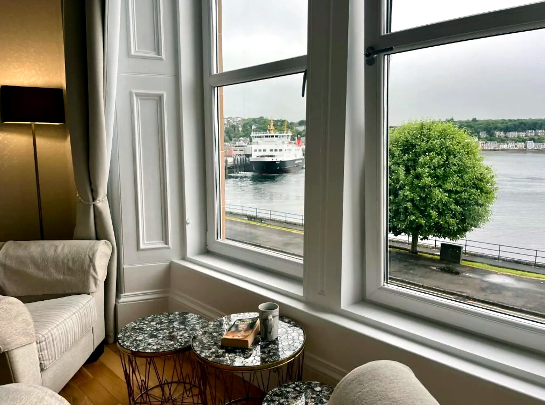 The Wemyss Bay ferry passing the window at Harbour View, seen past armchairs and a coffee table