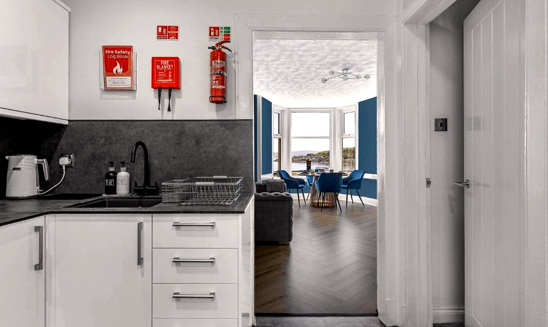 White kitchen with a view through to the blue sitting room and its sea-facing bay window