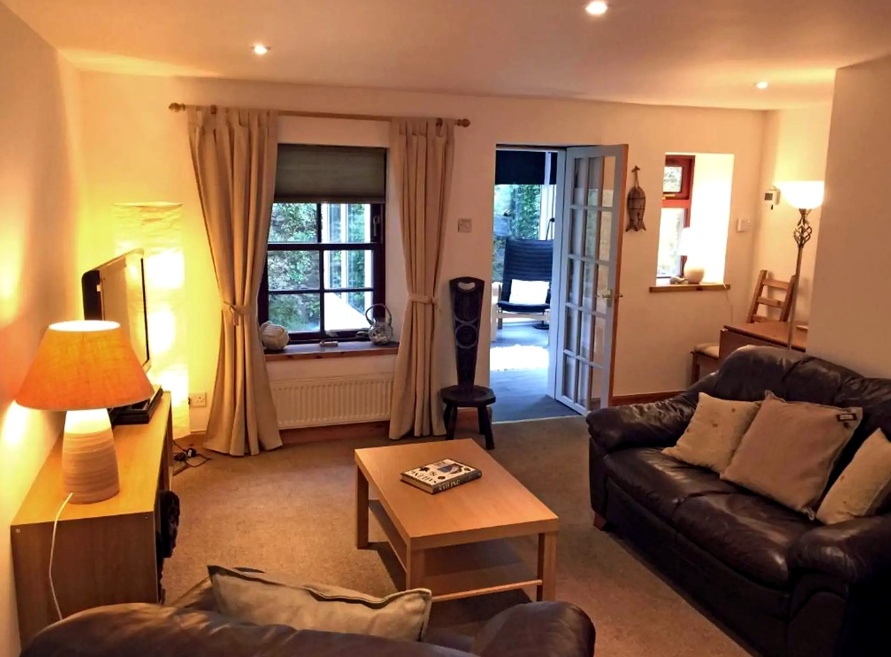 Warmly lit living room at Old Fisherman's Cottage with leather sofas and garden doors