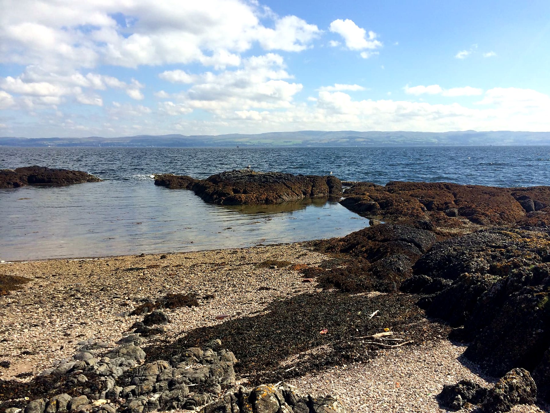 Shell-sand beach and tidal pool with the mainland hills beyond, Isle of Bute