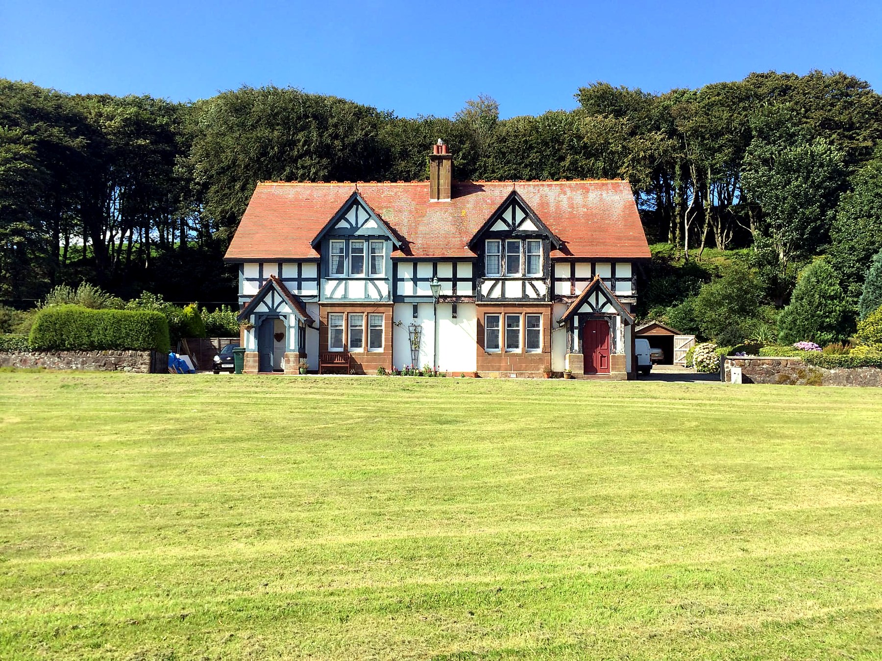 Red-roofed half-timbered estate cottage facing the green at Kerrycroy, Isle of Bute