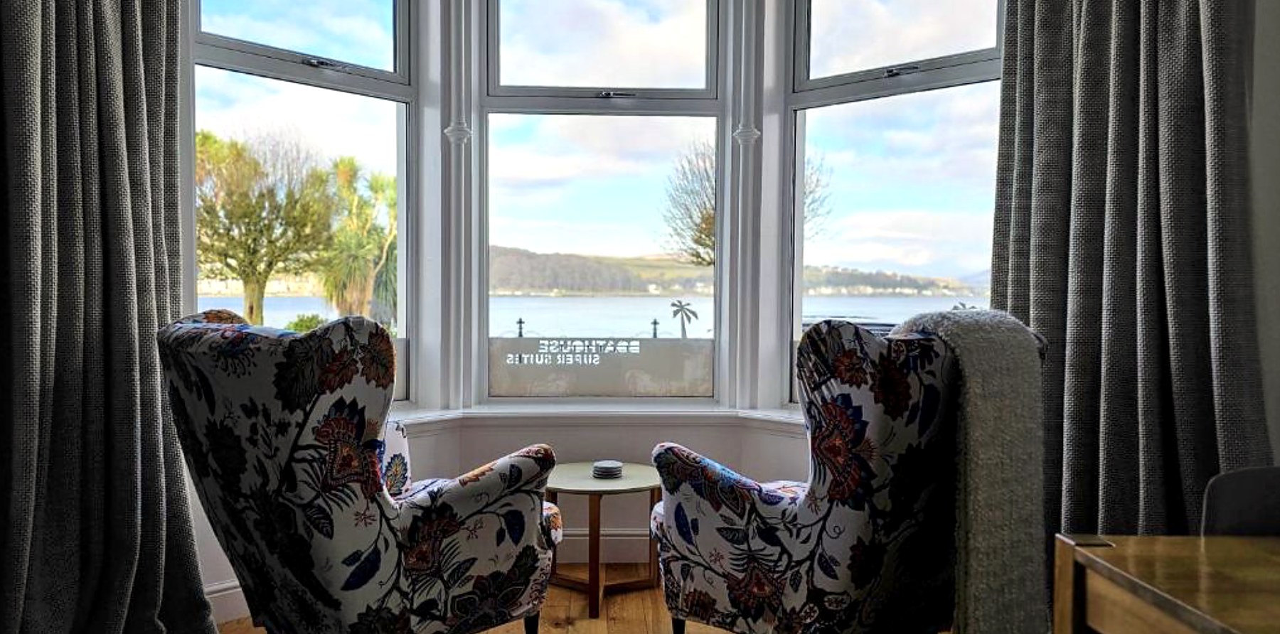 Two armchairs in a bay window at Boat House Super Suites looking over Rothesay Bay