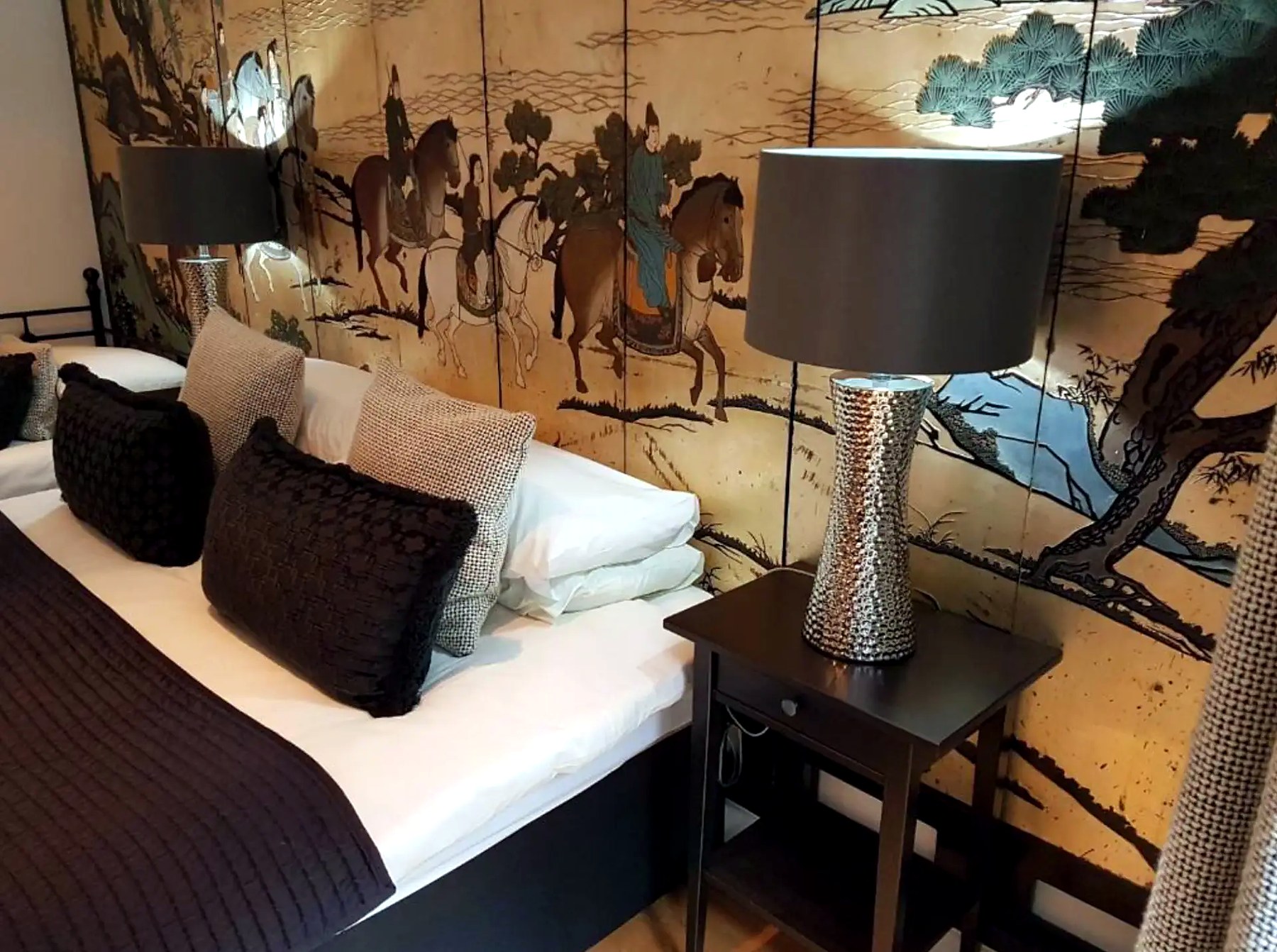 Bed at Boat House Super Suites set against a gold oriental screen with horses and pine trees