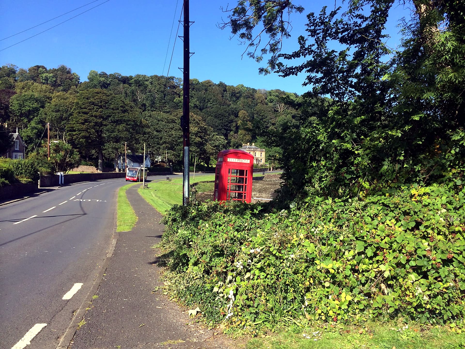 Red telephone box and island bus on a wooded village road on the Isle of Bute
