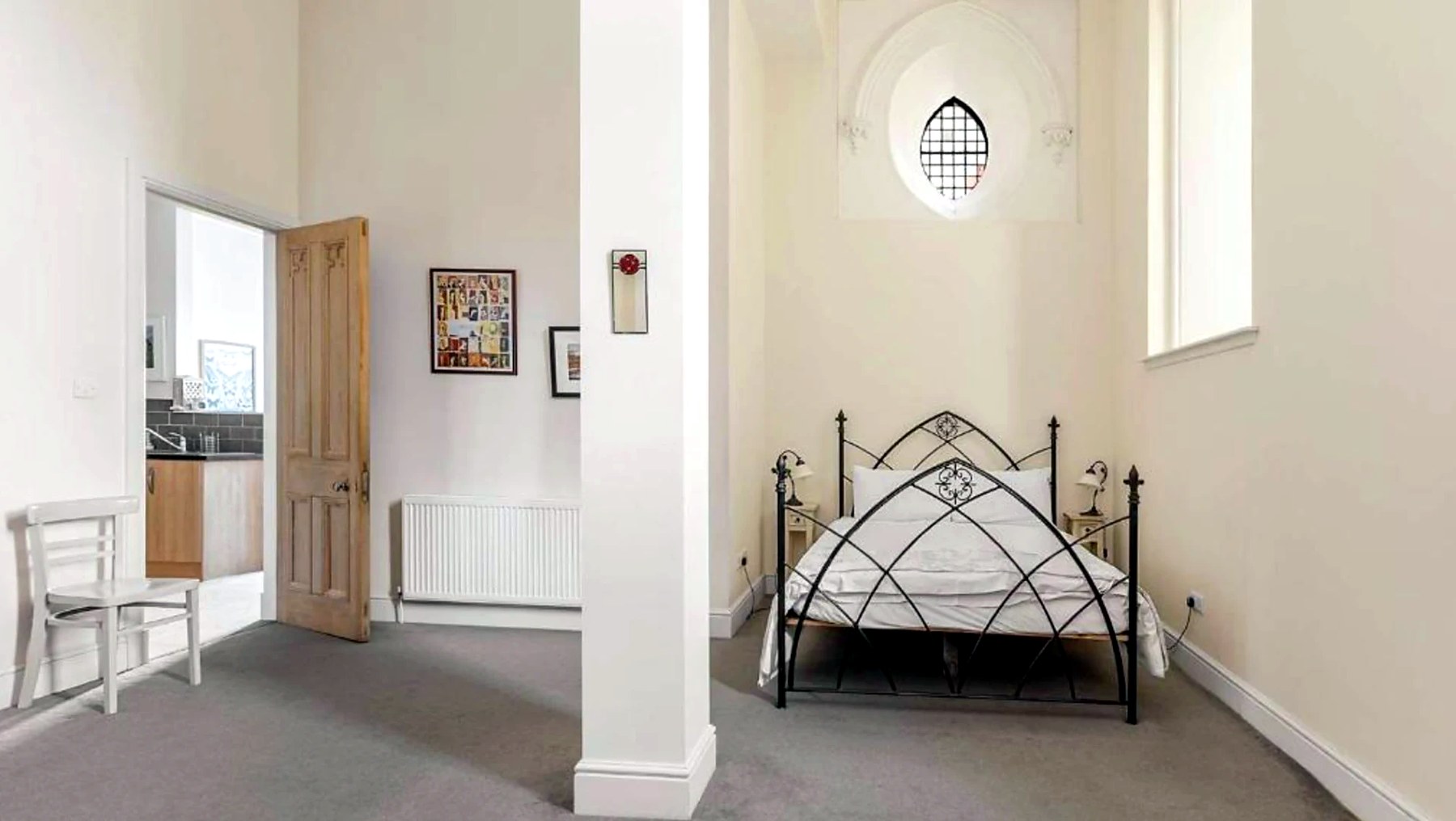 Double bedroom with black iron bedstead beneath an arched church window