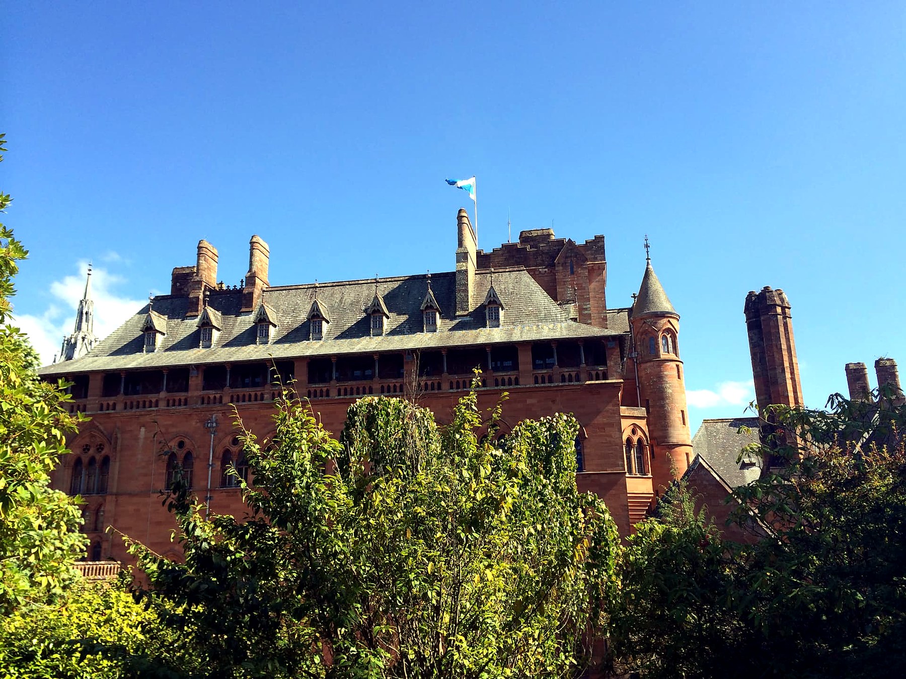 The red sandstone roofline and turret of Mount Stuart House on the Isle of Bute, with the Saltire flying above