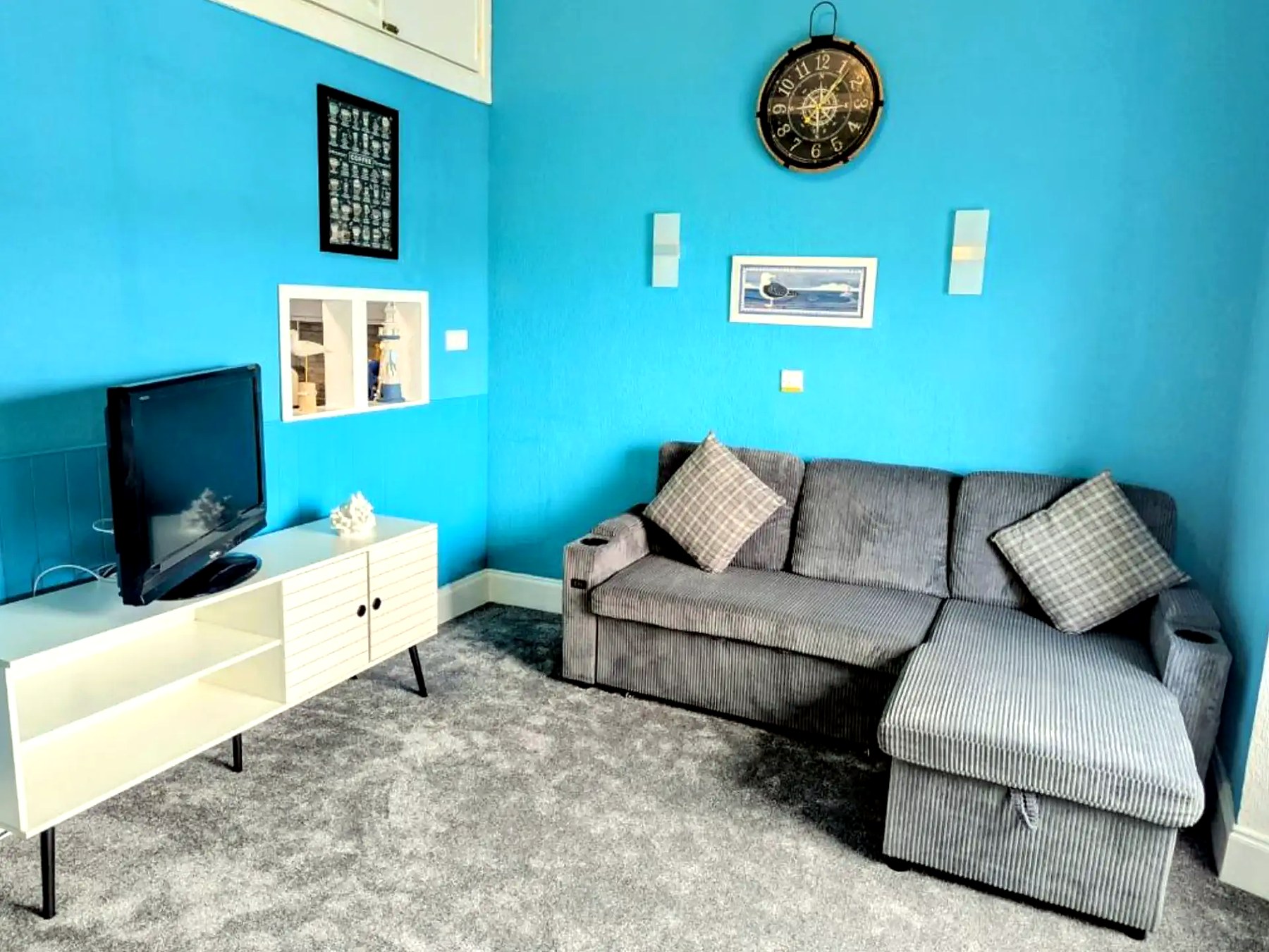 Bright sitting room in a Commodore apartment with a corner sofa and nautical clock