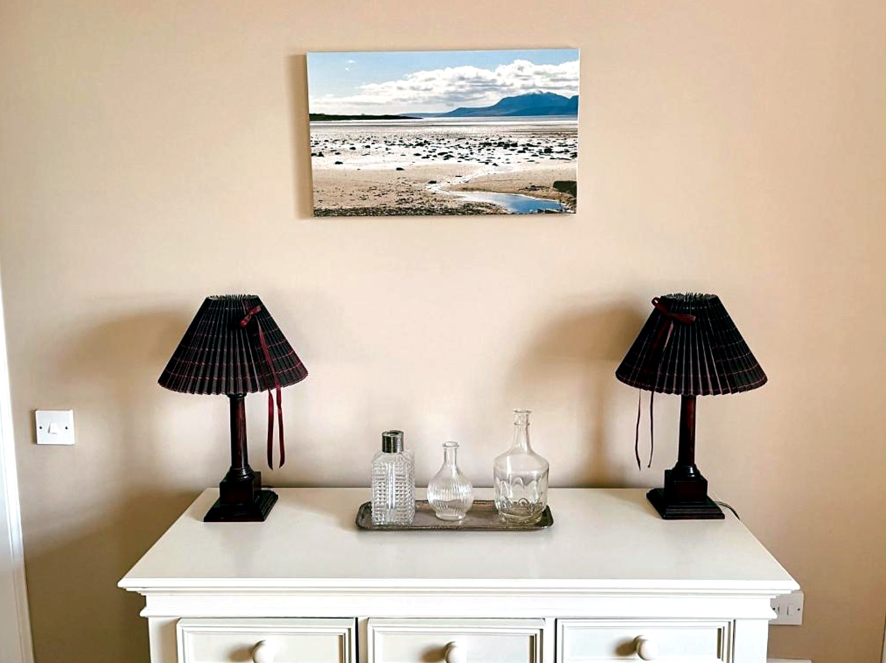 Bedroom dresser with paired lamps beneath a canvas print of a Bute beach
