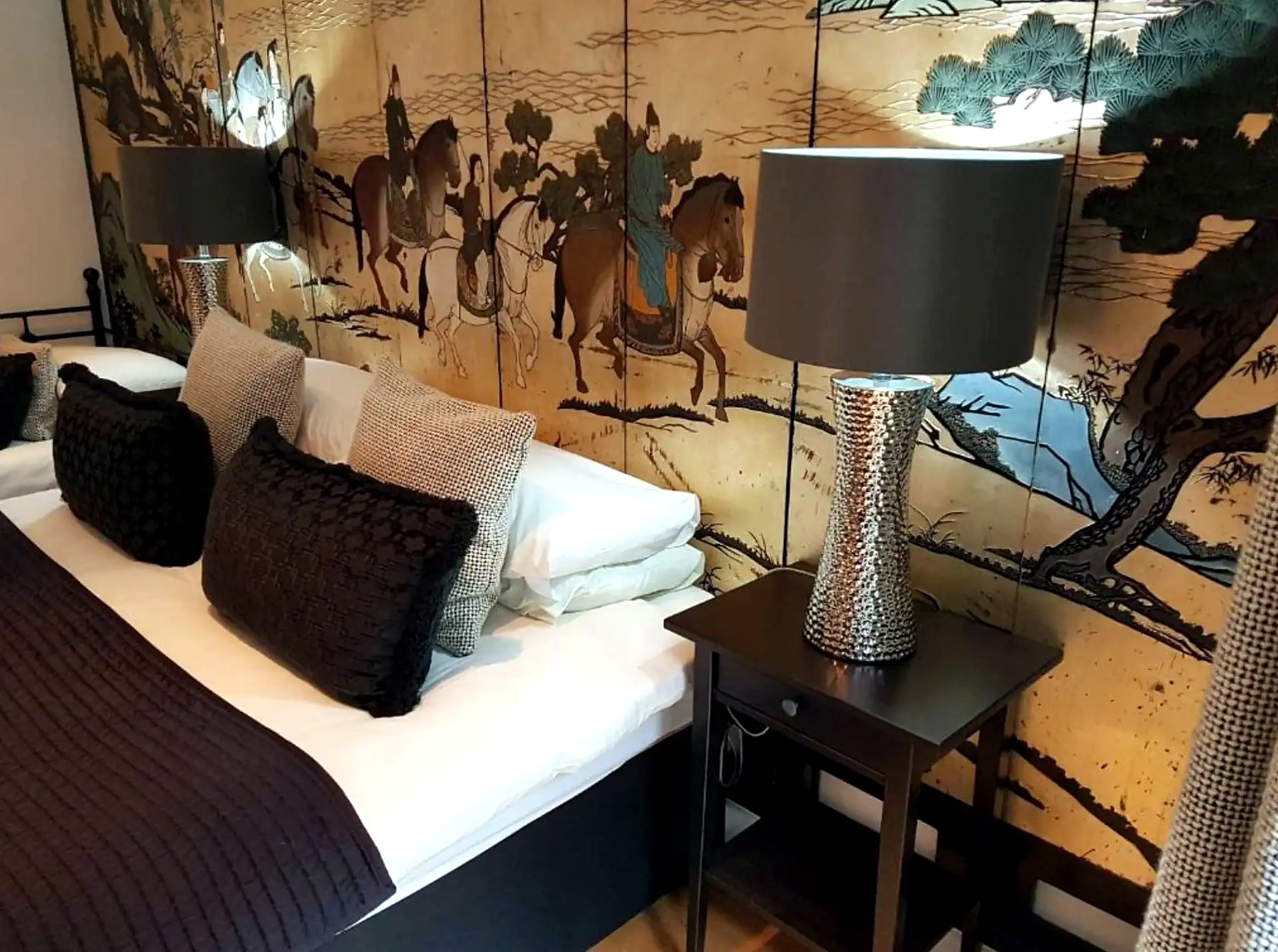 Bed with white linen and dark cushions against a gold oriental screen