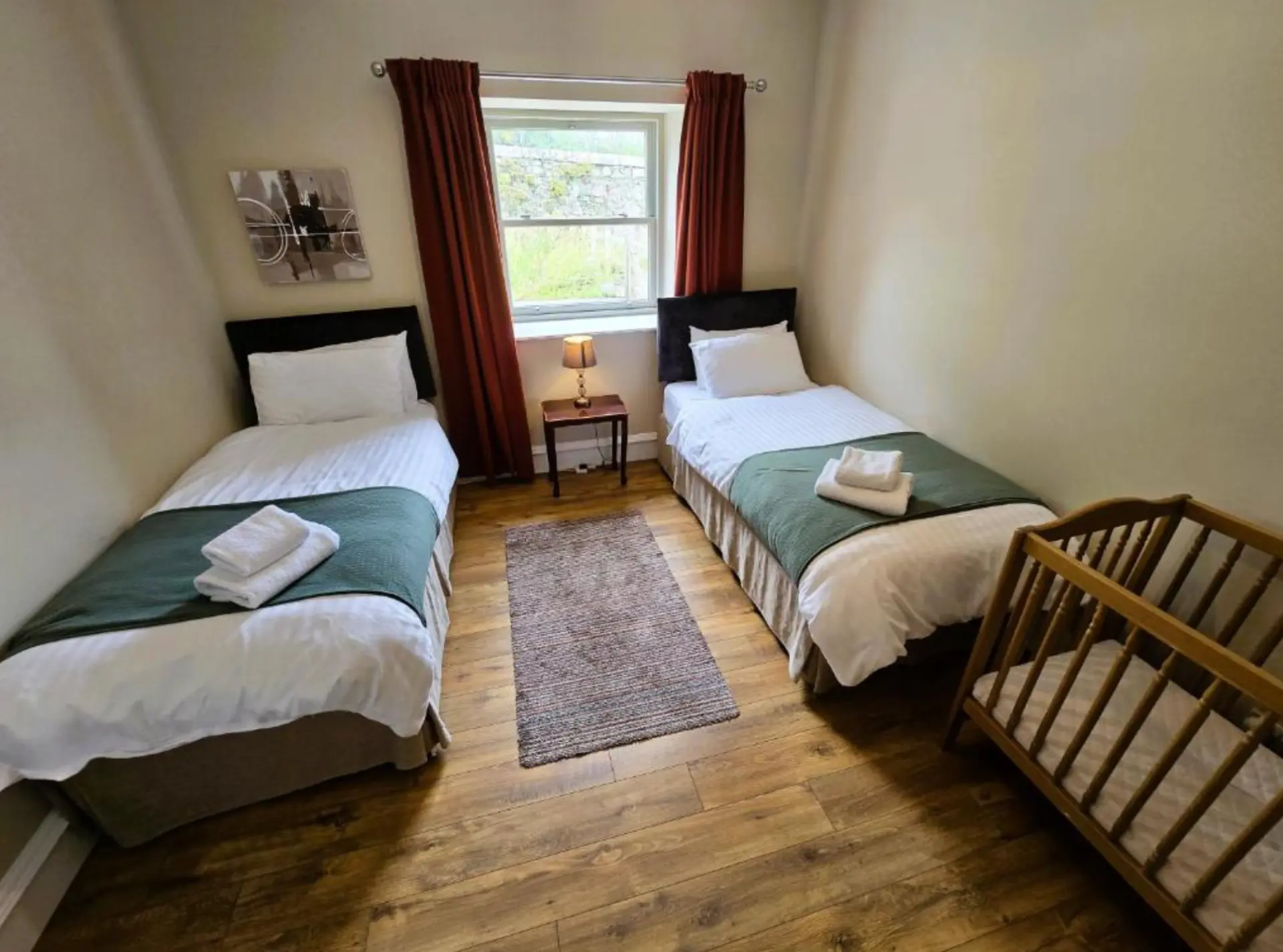 A twin bedroom at Balmory Stables with two beds, a cot and a window over the stone dyke
