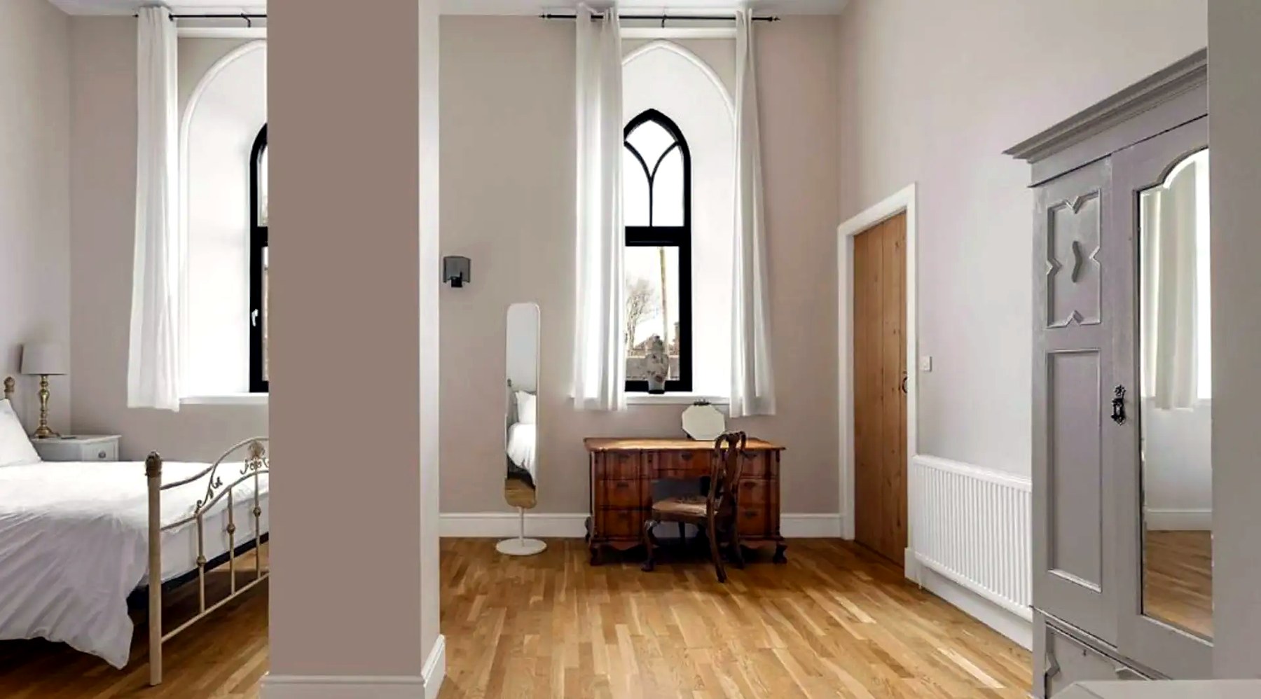 Bedroom in the converted church with tall Gothic arched windows, brass bed and oak floor