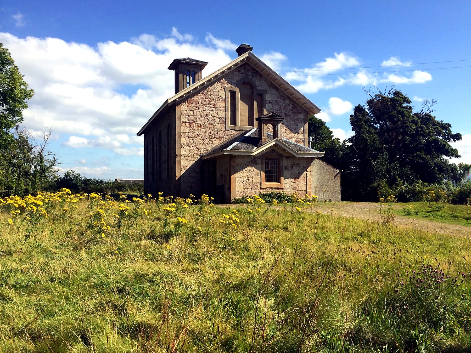 Disused sandstone church with a bell tower standing in a wildflower meadow on the Isle of Bute