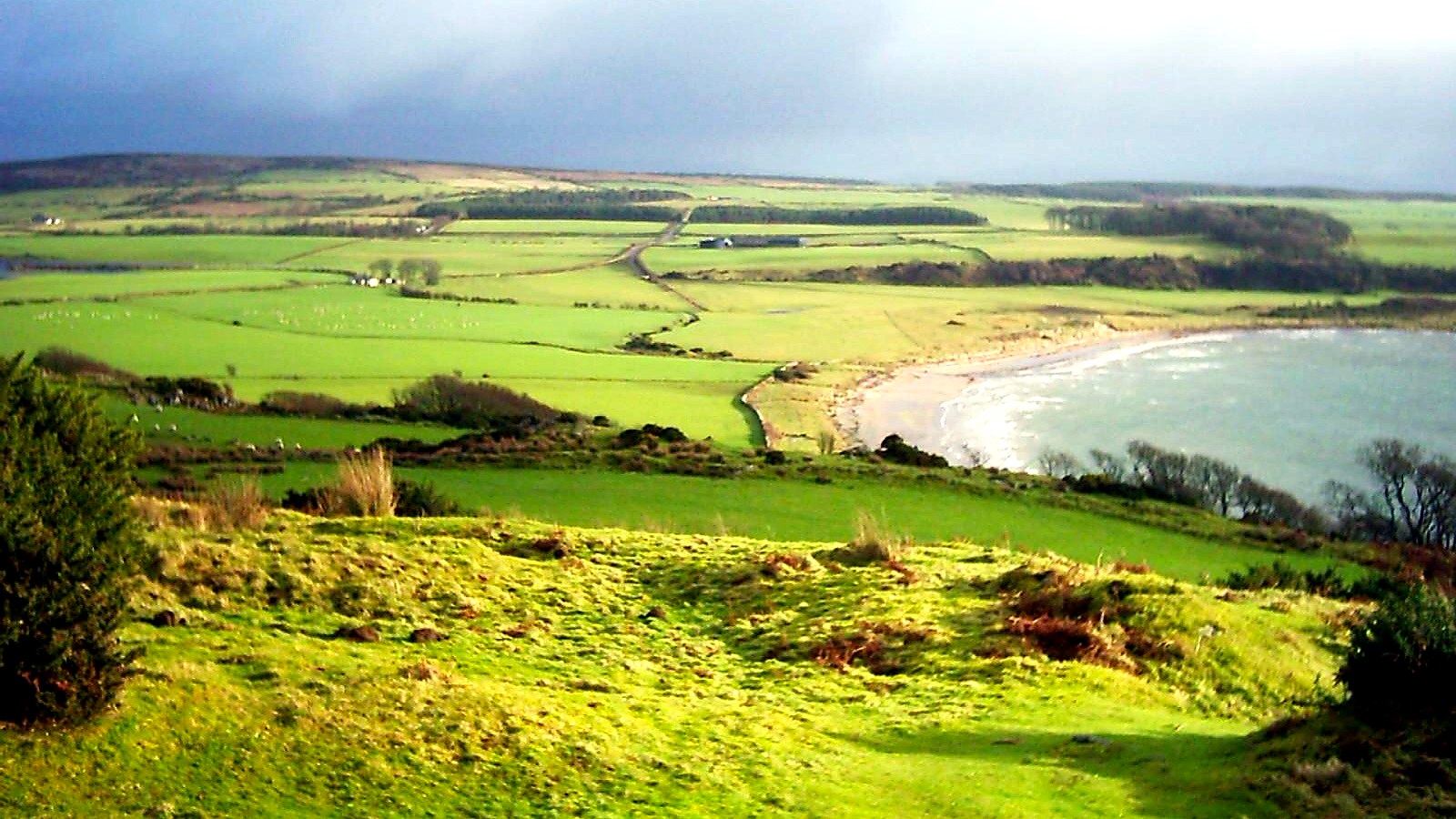 Green farmland and hedged fields sloping down to a sandy bay on the west coast of the Isle of Bute