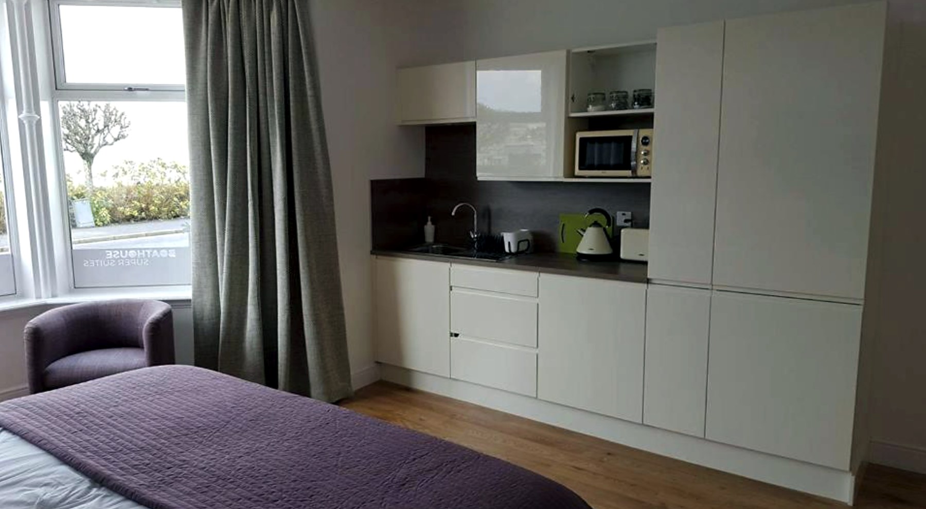 Suite at Boat House with a bed, armchair and a fitted white kitchenette along the wall