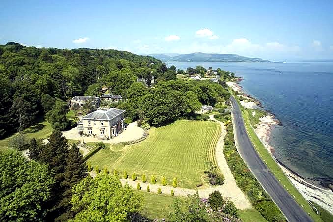 Aerial view of a country house in gardens beside the coast road on the Isle of Bute