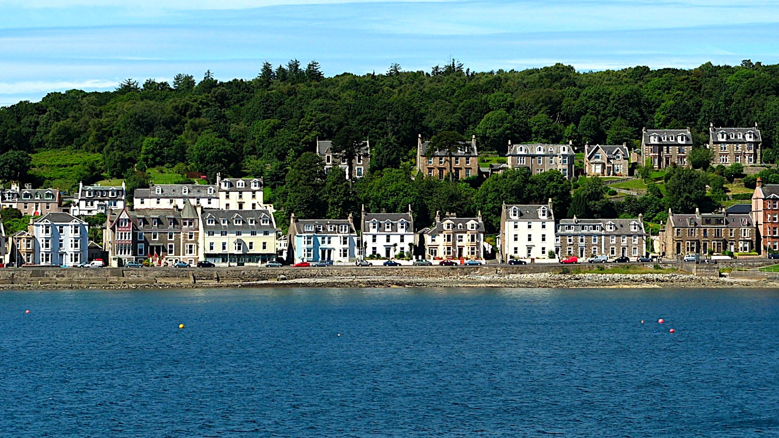 Row of Victorian seafront villas backed by woodland on the Isle of Bute, seen from the water