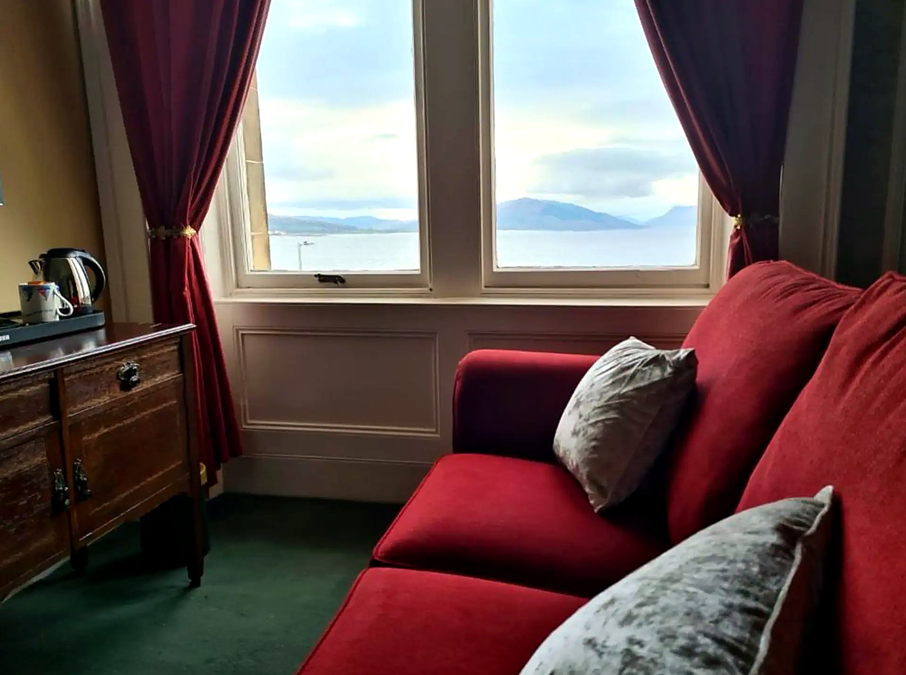 Guest lounge at St Ebba's with red sofas facing a bay window over the Firth of Clyde