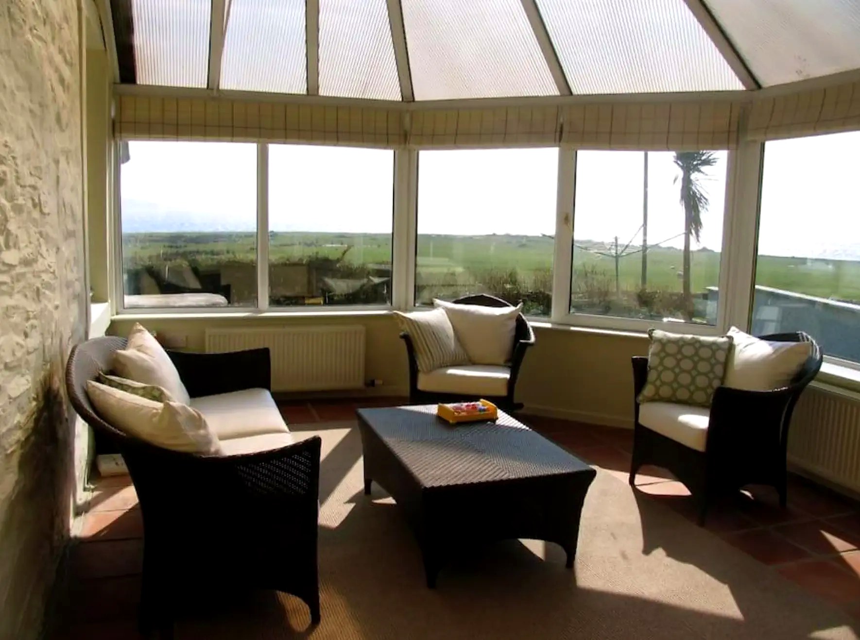 Sun room at The Old School House with wicker seating and views over fields to the sea