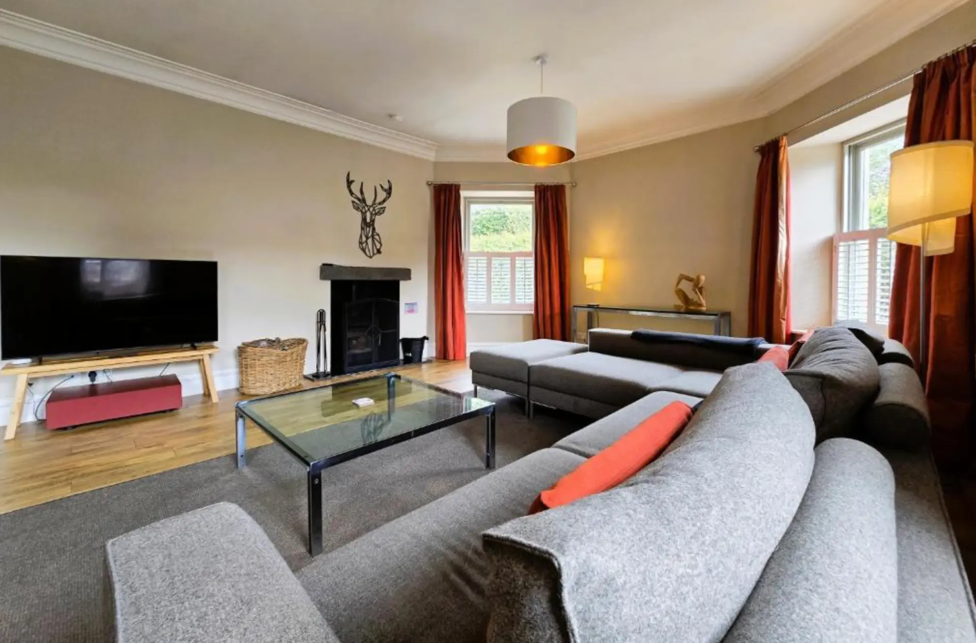 The lounge at Balmory Stables with a wood-burning stove, corner sofas and shuttered windows