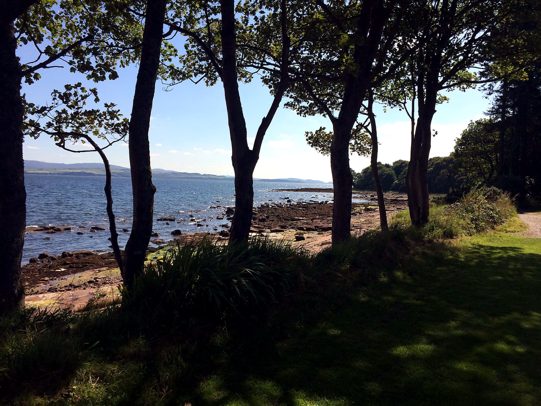 Red sandstone rocks and blue water framed by trees on the east coast shore path of the Isle of Bute