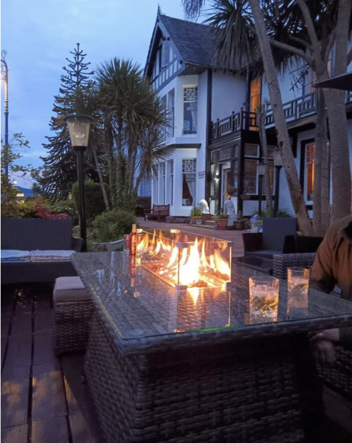A lit fire pit on the terrace at Battery Lodge at dusk, with the villa and palms behind