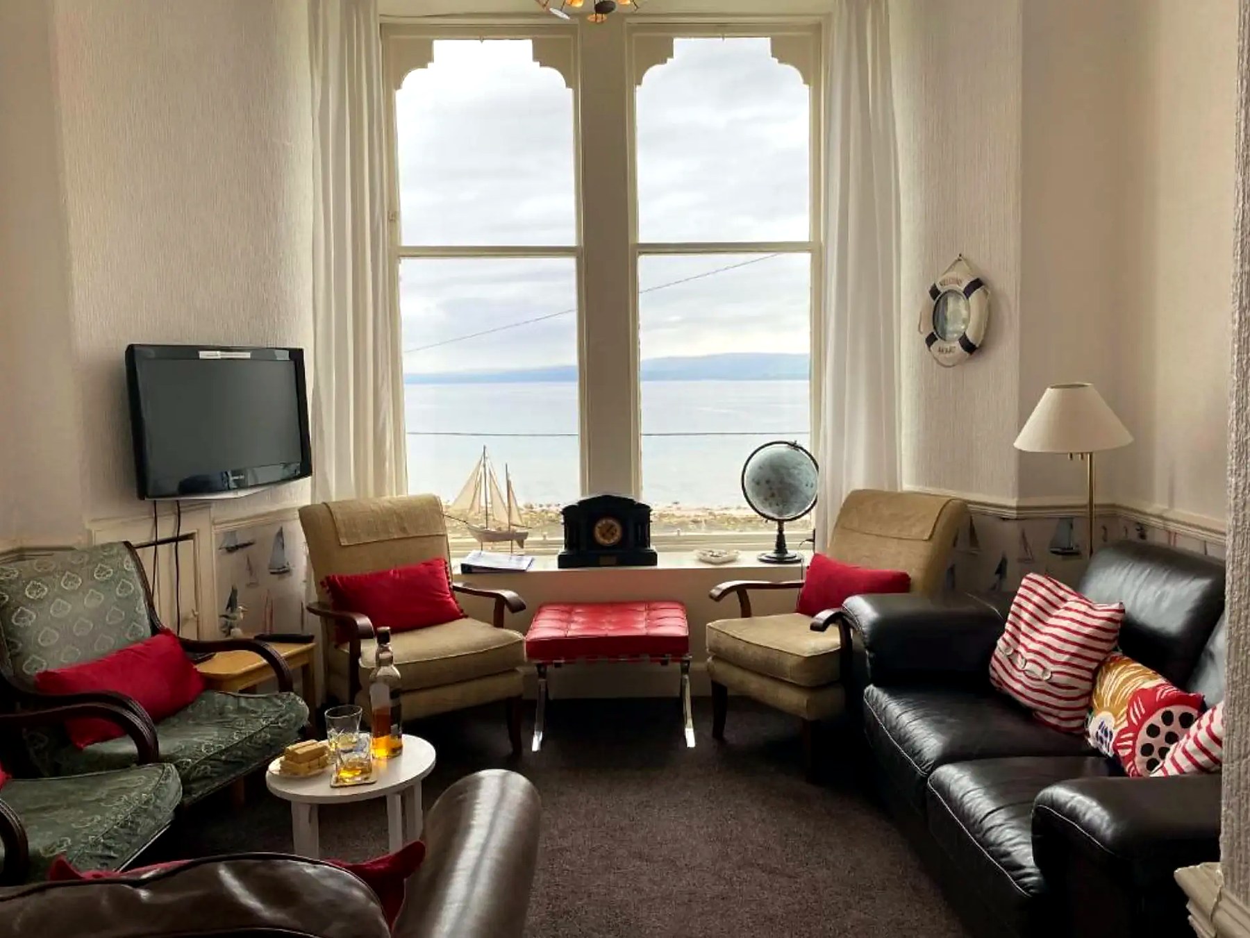 Armchairs facing a tall bay window with a sea view in the lounge at St Blanes House