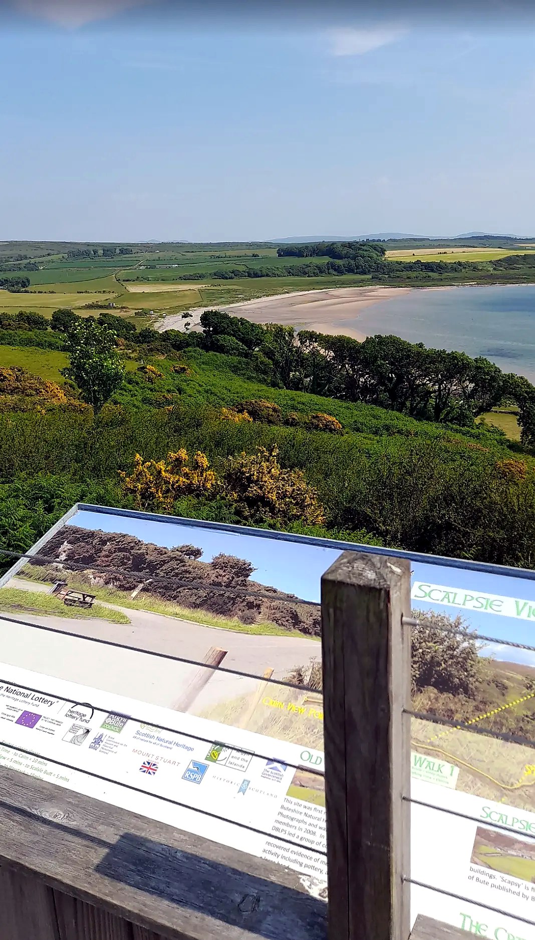 The Scalpsie Bay viewpoint interpretation board on the Isle of Bute, looking down over the beach and farmland to the sea