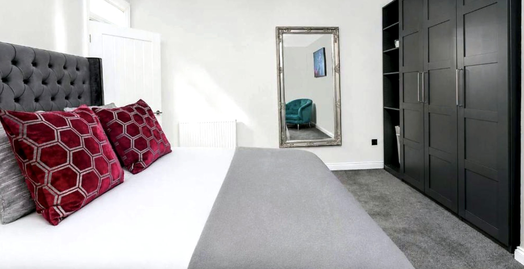 Bedroom with a tall silver mirror, dark wardrobes and a wide double bed