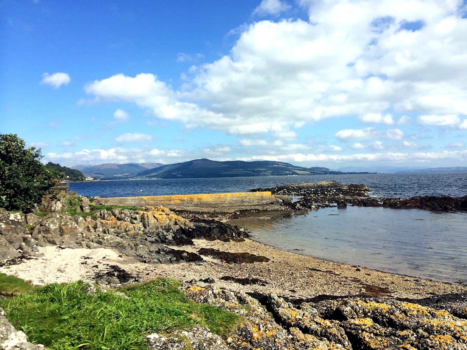 Small stone jetty, shingle beach and gulls with the mainland hills across the Firth of Clyde, Isle of Bute