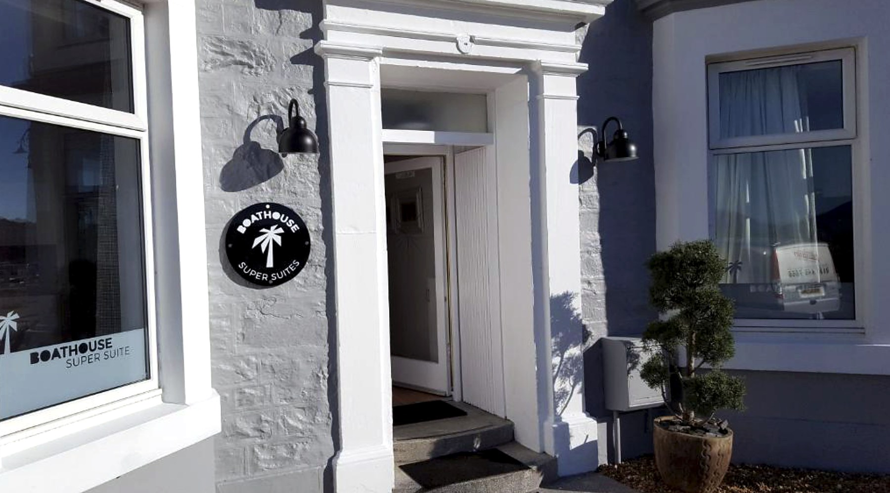 The Boat House Super Suites entrance with its palm-tree sign and lantern lights in Rothesay