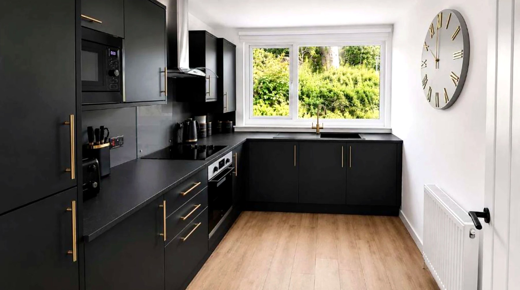 Matt black kitchen with brass handles and a garden window at Bayview at the Port